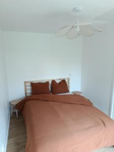 a bed with orange sheets and a ceiling fan at Maisonnette à la campagne in La Couyère