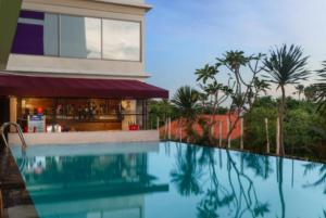 a swimming pool in front of a building with a bar at Quest Hotel Darmo - Surabaya by ASTON in Surabaya