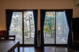 a room with two large glass doors with trees outside at Hideaway Hakone Sengokuhara in Sengokuhara