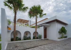 a white house with palm trees in front of it at Monstera Uluwatu in Uluwatu