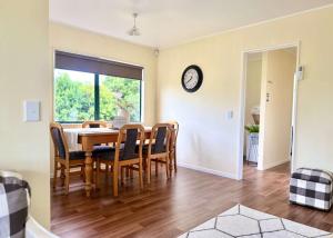 a dining room with a table and chairs and a clock at Peaceful Country Escape in Gordonton - Green Meadows Cottage in Taupiri