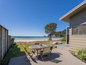 a patio with a table and chairs and the beach at Beachfront Beauty - Whangamata Beachfront Home in Whangamata