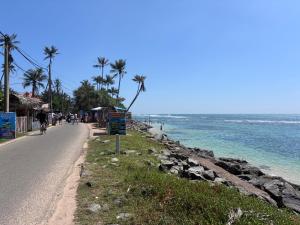 a road next to the ocean with palm trees at Handagedara Madiha Villa in Matara