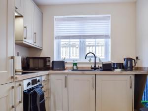 a kitchen with white cabinets and a sink and a window at The Old Dairy in Nether Broughton