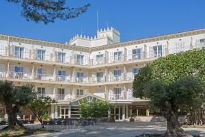 Un gran edificio blanco con árboles delante. en Hotel Castell dels Hams, en Porto Cristo