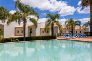 a swimming pool with blue chairs and palm trees at Quinta Sao Roque Townhouses in Lagos