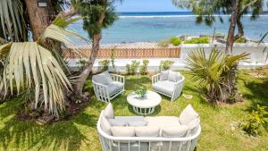 a patio with white chairs and a table and the beach at La Villa Bleue, Pieds dans l'eau in Saint-Leu