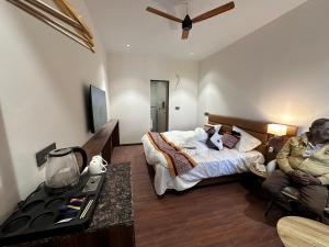 a man sitting next to a bed in a room at Hulara Meadows in Lucknow +3 photos