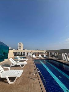 a pool on the roof of a building with lounge chairs at Prime Flat Palladium Mar & Piscina in São Vicente