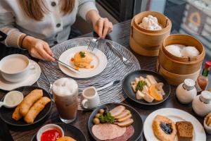 a table with plates of food and a person holding a fork at Avani Ratchada Bangkok Hotel in Bangkok