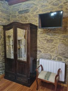 a tv on a stone wall with a cabinet and a chair at A Regueira Habitaciones in Alján