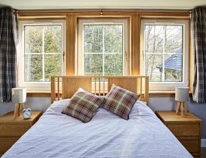 a bedroom with a bed with two pillows and two windows at Glenalbyn Cottage in Saint Fillans +32 photos