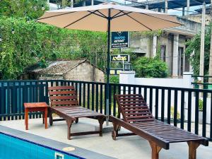 two wooden chairs and an umbrella next to a pool at Lotus Manuvala - Negombo in Kochchikade