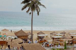 a beach with umbrellas and a palm tree and the ocean at Ayooka Beach Residence Grand Bassam in Grand-Bassam