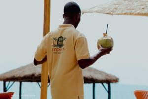 a man in a yellow shirt holding a coconut at Ayooka Beach Residence Grand Bassam in Grand-Bassam