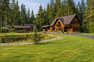 a large wooden house with a pond and trees at Két Patak Retreat in Bucsin