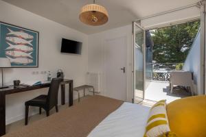 a bedroom with a bed and a desk and a balcony at Logis Hôtel de la Pointe du Cap Coz in Fouesnant