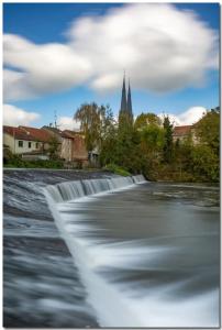 a river with a waterfall with a church in the background at Chambre d hote in Sarralbe