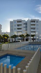 a swimming pool with a white fence and a building at Apartment steps away from the beach in La Serena