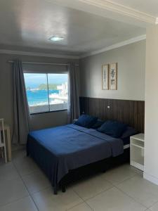 a bedroom with a blue bed and a large window at Residencial Costa Marfim in Bombinhas