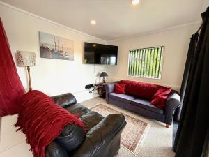a living room with a leather couch and red blankets at Cosy Raglan Studio - Walk to Beach and Village - Roberts St - Studio Downstairs in Raglan