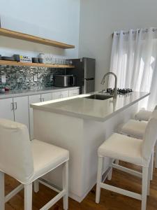 a white kitchen with a sink and white chairs at Island Time house in Utila