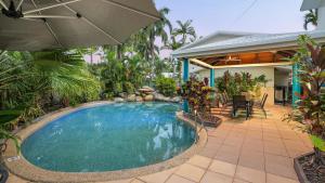 a swimming pool in front of a house with an umbrella at Trinity Beach Pacific in Trinity Beach