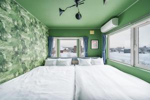 two white beds in a green room with a window at The Crane Sanctuary Kamifurano in Kami-furano