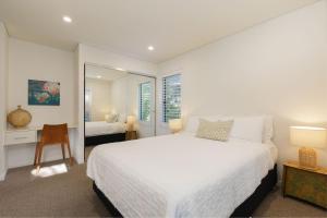 a white bedroom with a large bed and a mirror at Waves #9 by Discover Stradbroke in Point Lookout