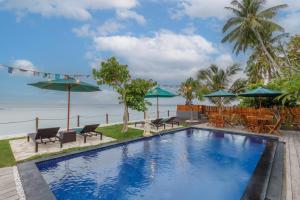 a swimming pool with chairs and umbrellas next to the ocean at La Semaya Beach Villas in Nusa Penida