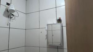 a white tiled bathroom with a mirror and a light at Pousada RC Q2 in Várzea Grande