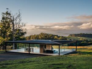 a glass house with a black roof on a field at Triptych - The Glass House in Koonya
