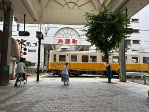 a woman standing on a sidewalk in front of a train at Nagi Takamatsu 702 in Takamatsu