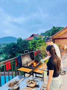 a man and woman cooking food on a grill at Cúc Phương Mebi Hotel in Phủ Nho Quan