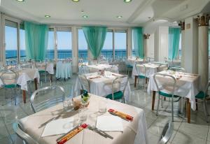 a restaurant with white tables and chairs and windows at Hotel Lido in Gabicce Mare