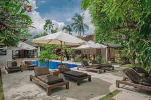 a patio with chairs and an umbrella and a pool at Frangipani Beach Hotel in Lovina