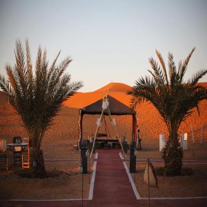a tent in the middle of a desert with two palm trees at hagra luxury camp Merzouga in Merzouga