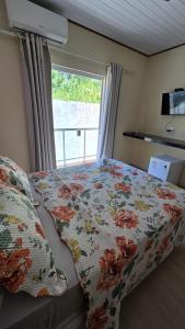 a bedroom with a bed with a flowered blanket and a window at Pousada Colibri in Trindade
