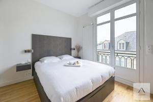 a bedroom with a large white bed with a large window at Le Palais du Commerce in Rennes