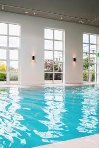 a swimming pool with blue water in a room with windows at Van der Valk Hotel Apeldoorn in Apeldoorn