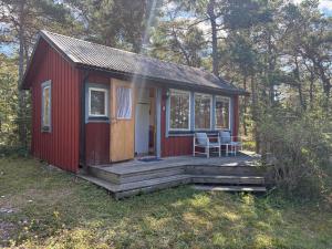 a red tiny house with a porch in the woods at Liten stuga med havsutsikt in VBY