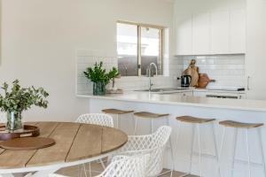 a white kitchen with a wooden table and chairs at The Water House - Lakeside Serenity & Modern Comfort in Encounter Bay