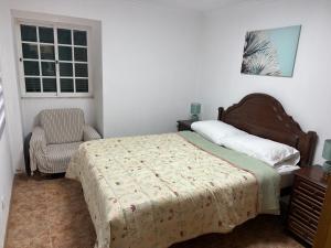 a bedroom with a bed and a chair and a window at Apartamento Caminho da Praia in Pedro Miguel