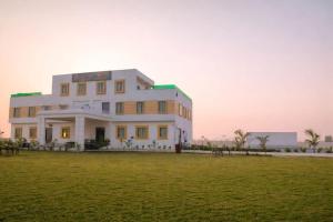 a white building with a field in front of it at Pushp Vatika Hotel & Resort in Thālera