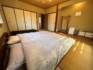 a bedroom with a large bed with white sheets at 一棟丸ごと貸別荘あそべるごでぃふーぞ in Takamori