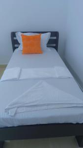 a white bed with an orange pillow on it at NyaliHomes in Mombasa