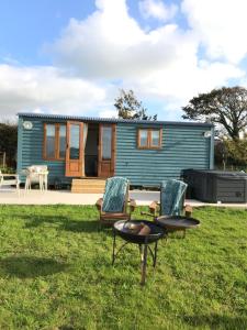 a blue tiny house with chairs and a table at Ty Beti at Gorlan yr Efail Shepherds Hut with Private Hot Tub in Holyhead