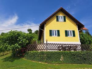 a yellow house with green windows and a fence at Ferienhaus Weingut Bauer in Gamlitz