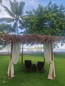 two chairs under a gazebo with a tree and the ocean at Pousada Vila da Barra in Ilha de Boipeba
