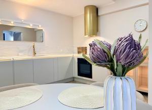 a white vase with purple flowers sitting on a table at Apartamenty Polna Park in Duszniki Zdrój +86 photos